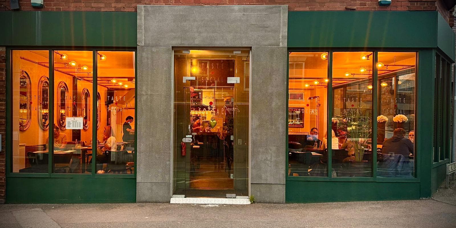The Taste Social storefront at night, glowing with warm interior light